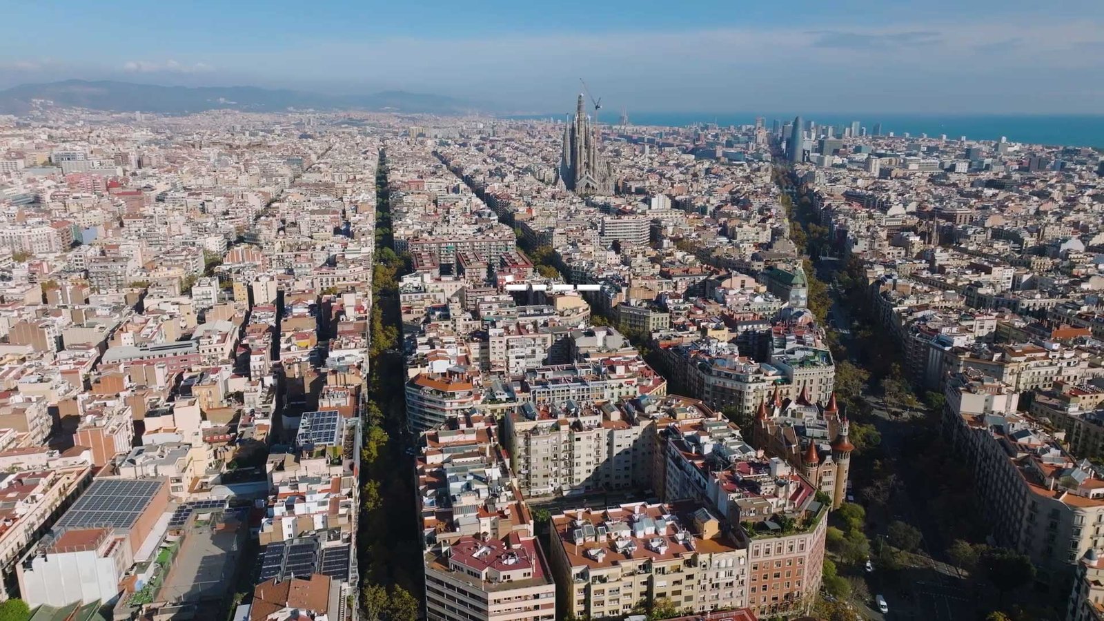Aerial drone view over Barcelona's Eixample grid, with the Sagrada Família in the distance